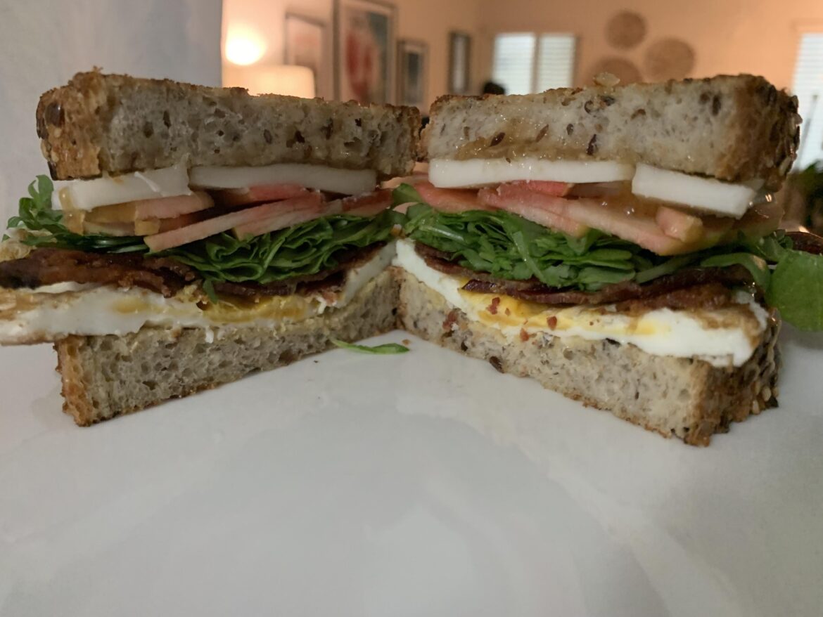 Breakfast sandwich inspired by the season - egg, bacon, goat’s milk Gouda, pink apple, arugula, and apple horseradish jam.