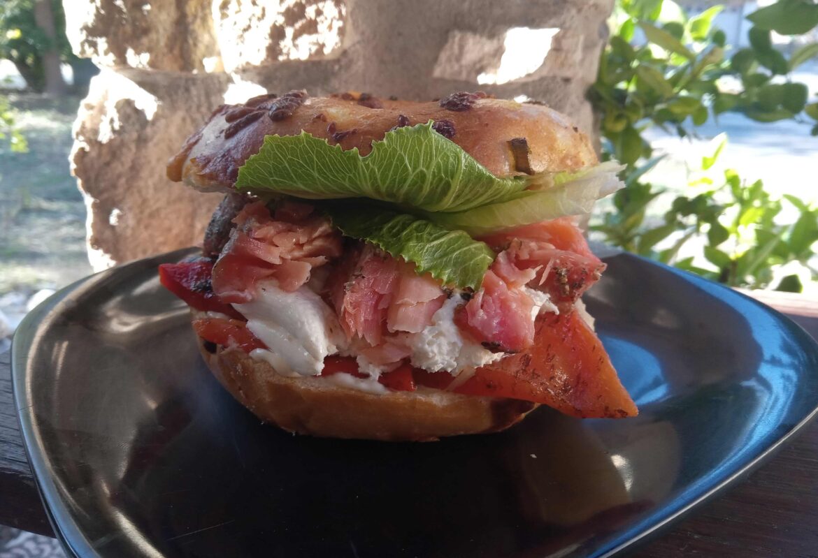 Home-cured and warm-smoked salmon (cured with added beet juice), whipped cream cheese, and roasted red peppers on a lightly-toasted cheese bagel.