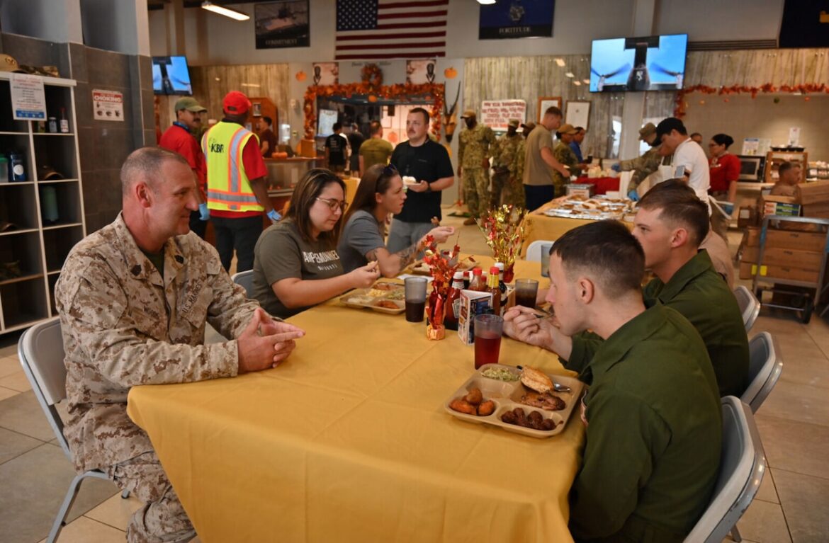 Defense Logistics Agency Troop Support Serves Thanksgiving Around the World > U.S. Department of Defense > Story A uniformed service member sits at a table while several others eat.