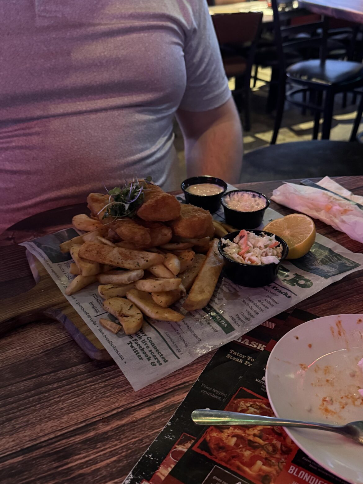 Fish and chips on a cutting board and the newspaper is already soaked through
