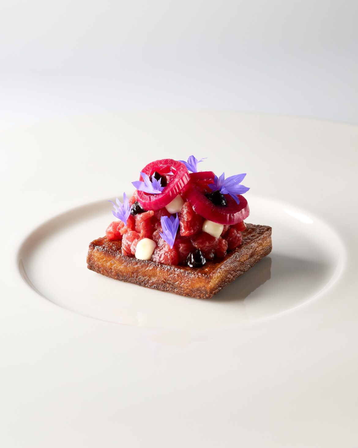 Potato cake fried in duck fat. Beef tenderloin marinated in olive oil, fish sauce, and Worcestershire sauce. Anchovy mayonnaise. Fermented garlic ketchup. Salt-baked egg yolk. Topped with red onion pickled in champagne vinegar and beetroot juice.