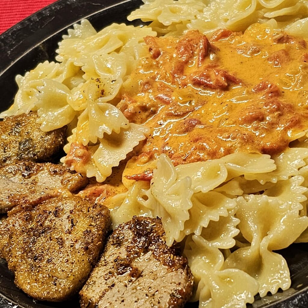 Schnitzel served with farfalle at a creamy white wine sauce with bacon, onions, chili peppers, and tomatoes