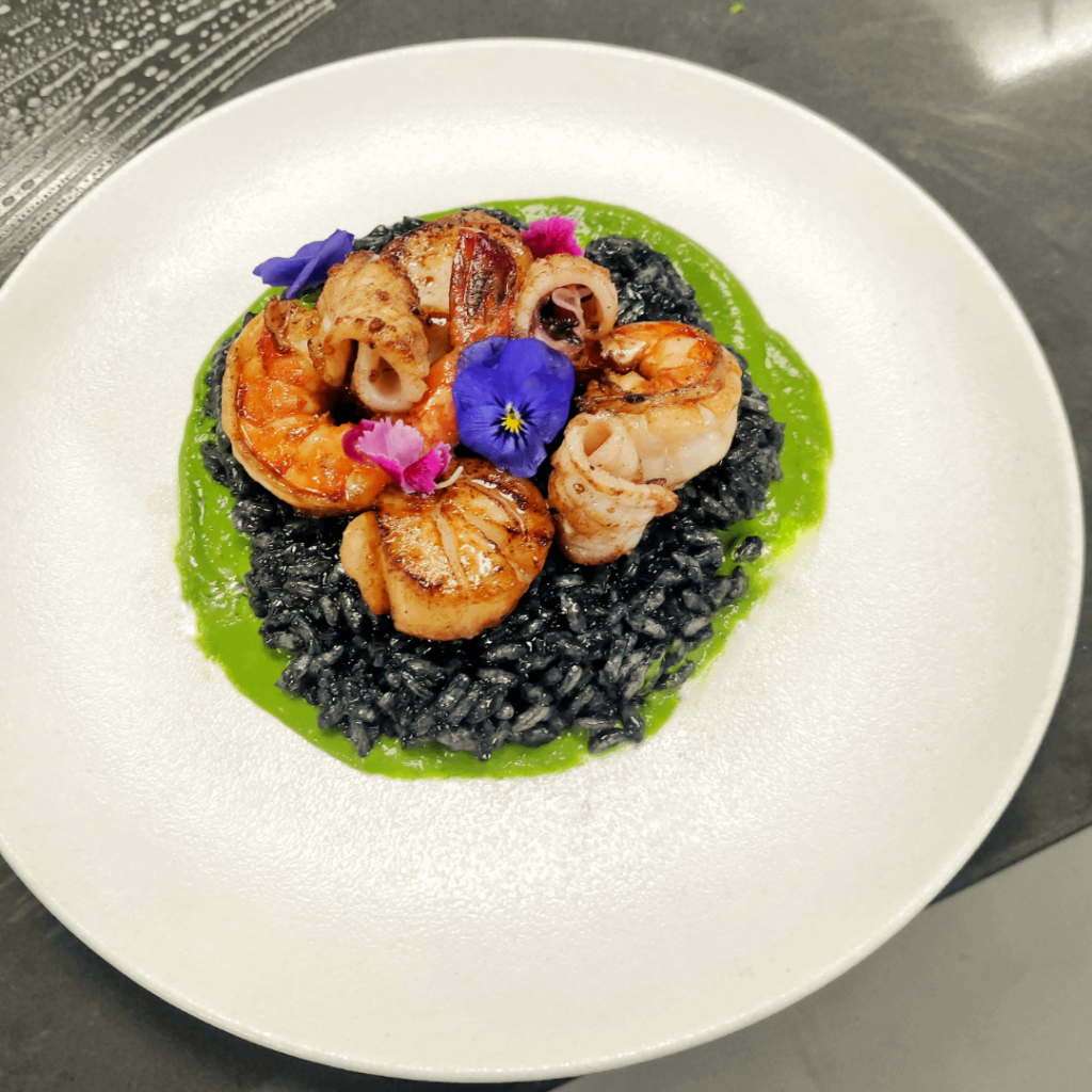 Squid ink risotto with parsley sauce, shrimps, scallops and fresh calamari