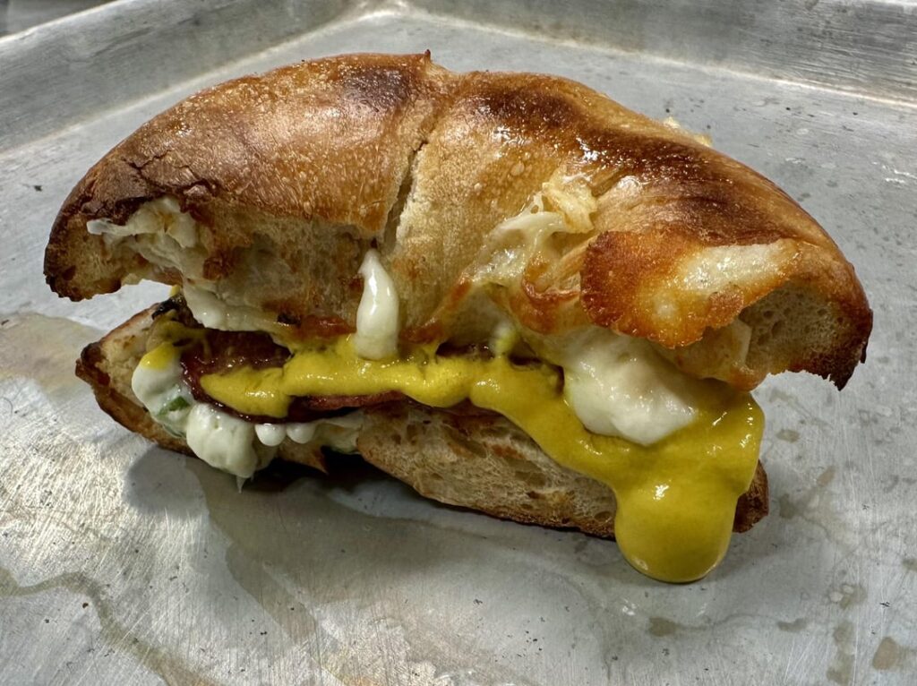 Salami, cheddar,  herb cream cheese and mustard on a bagel.