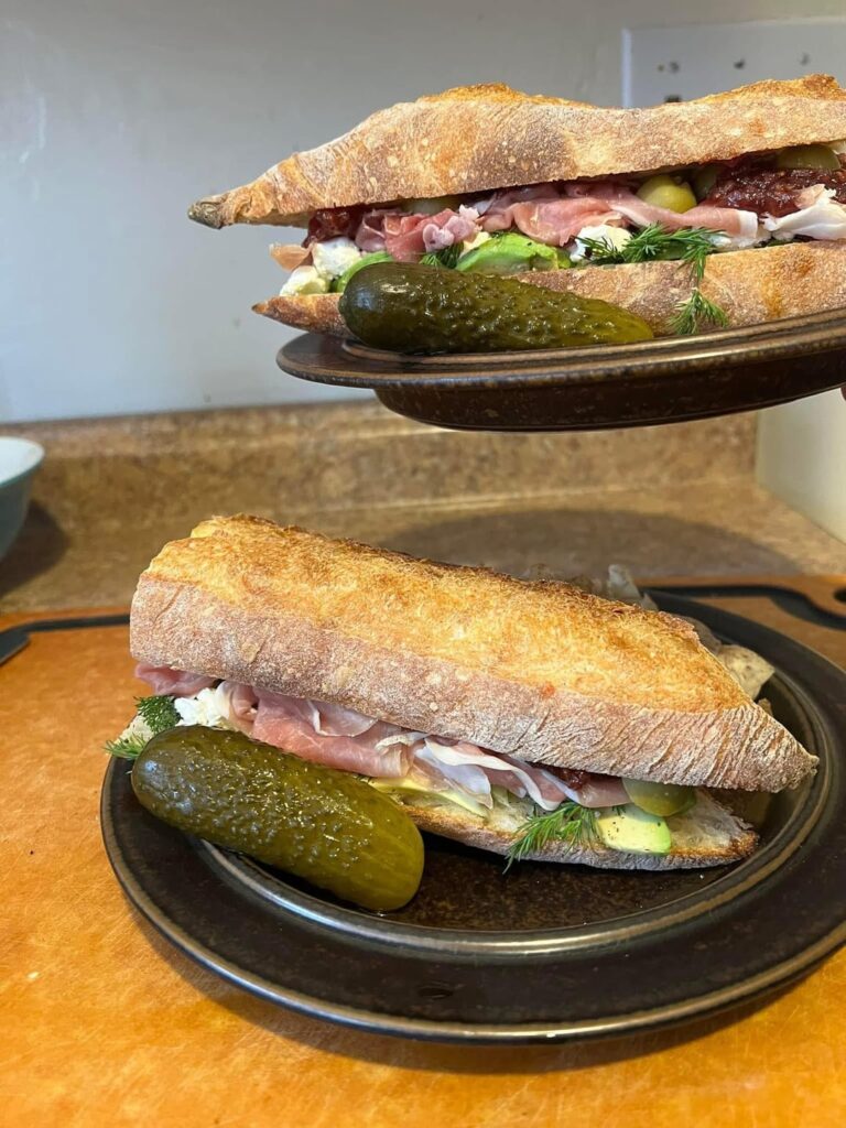 Prosciutto, avocado, cypress grove purple haze goat cheese, dill, sliced red pepper stuffed olives, primo raspberry habanero jam ancienne baguette sandwich with taro chips and a bubbies pickle Prosciutto, avocado, cypress grove purple haze goat cheese, dill, sliced red pepper stuffed olives, primo raspberry habanero jam ancienne baguette sandwich with taro chips and a bubbies pickle