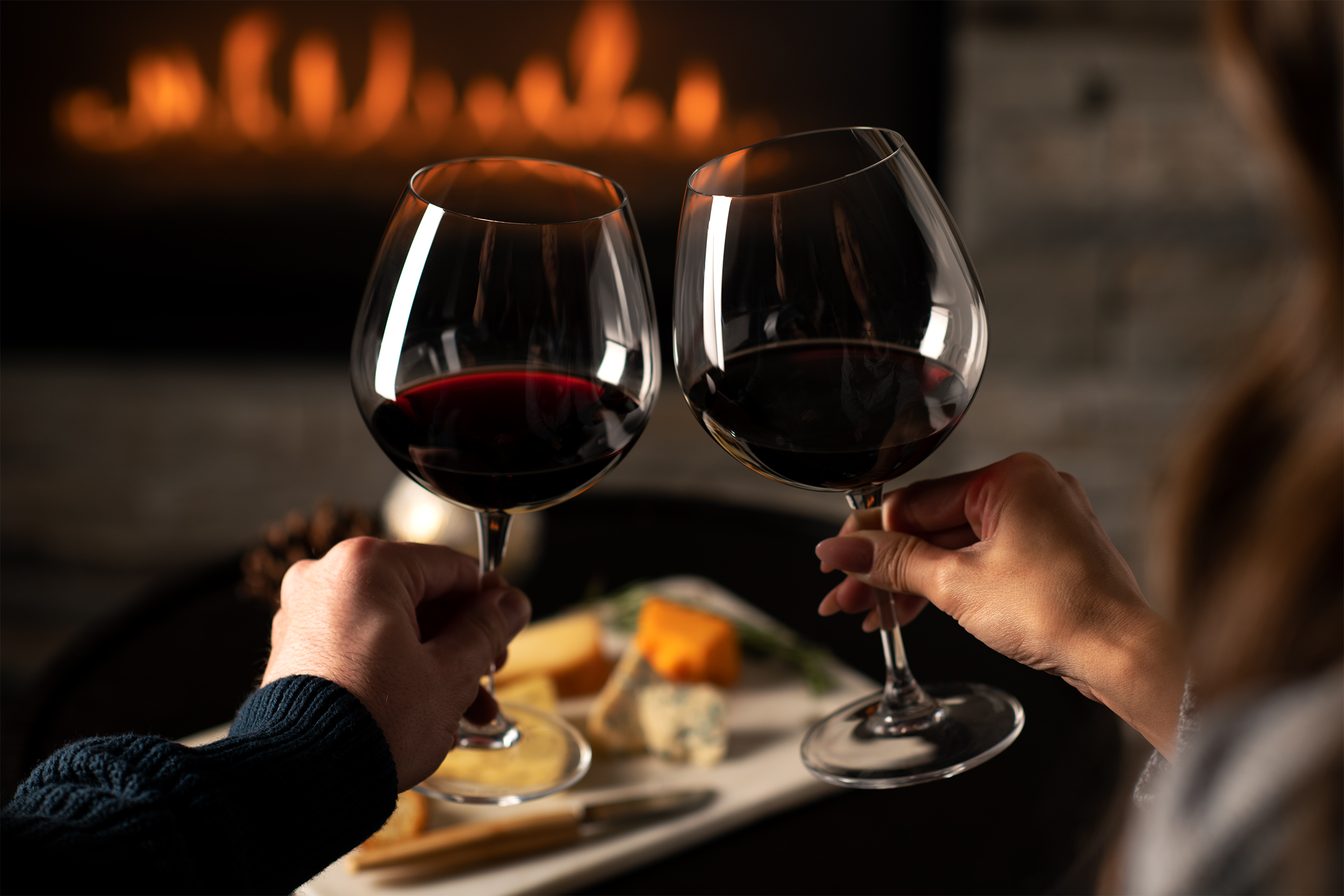 Couple toasting with red wine in front of a fireplace.