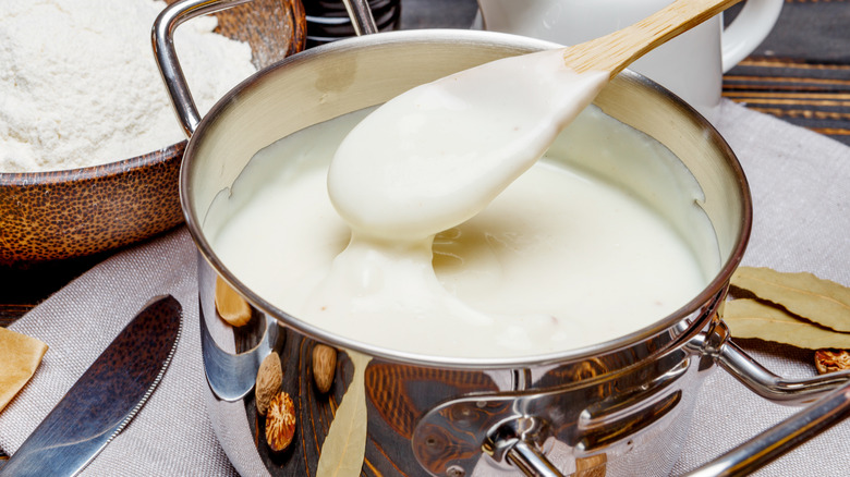 Béchamel sauce in a pan, with spoon being lifted out