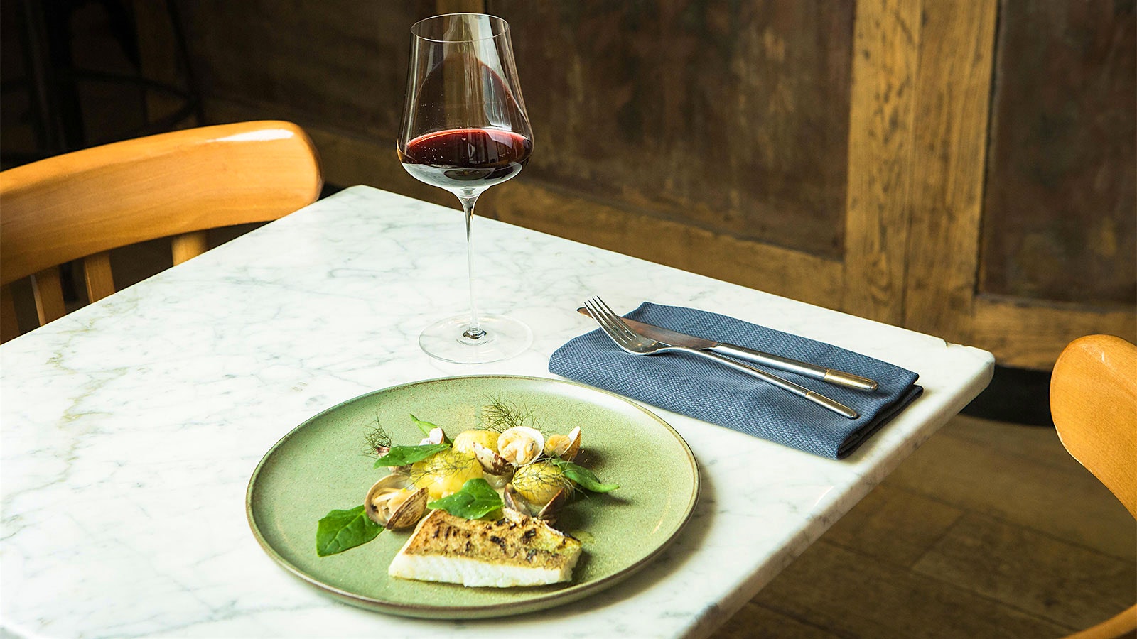  Dish of fish, clams and fresh herbs from Vantre in Paris, next to a glass of red wine