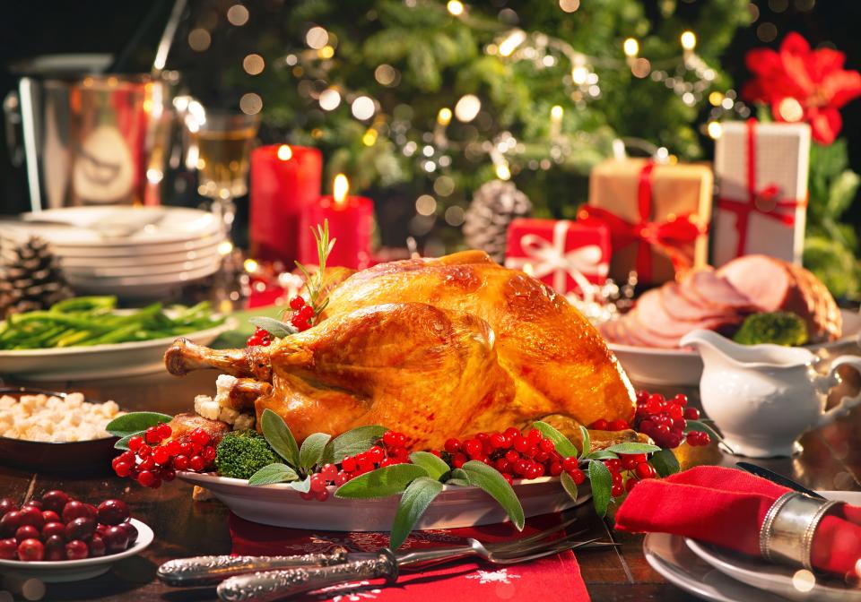 A Christmas turkey dinner garnished with red berries and sage leaves in front of a Christmas tree and burning candles.