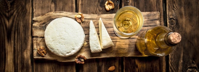 A close-up of some appetizing sheep cheese alongside a glass and bottle of white wine.
