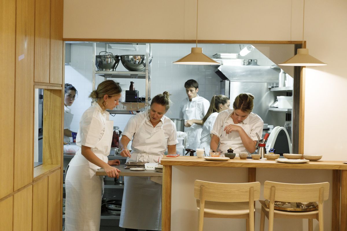 Chefs at work in an open kitchen lined with light wood.