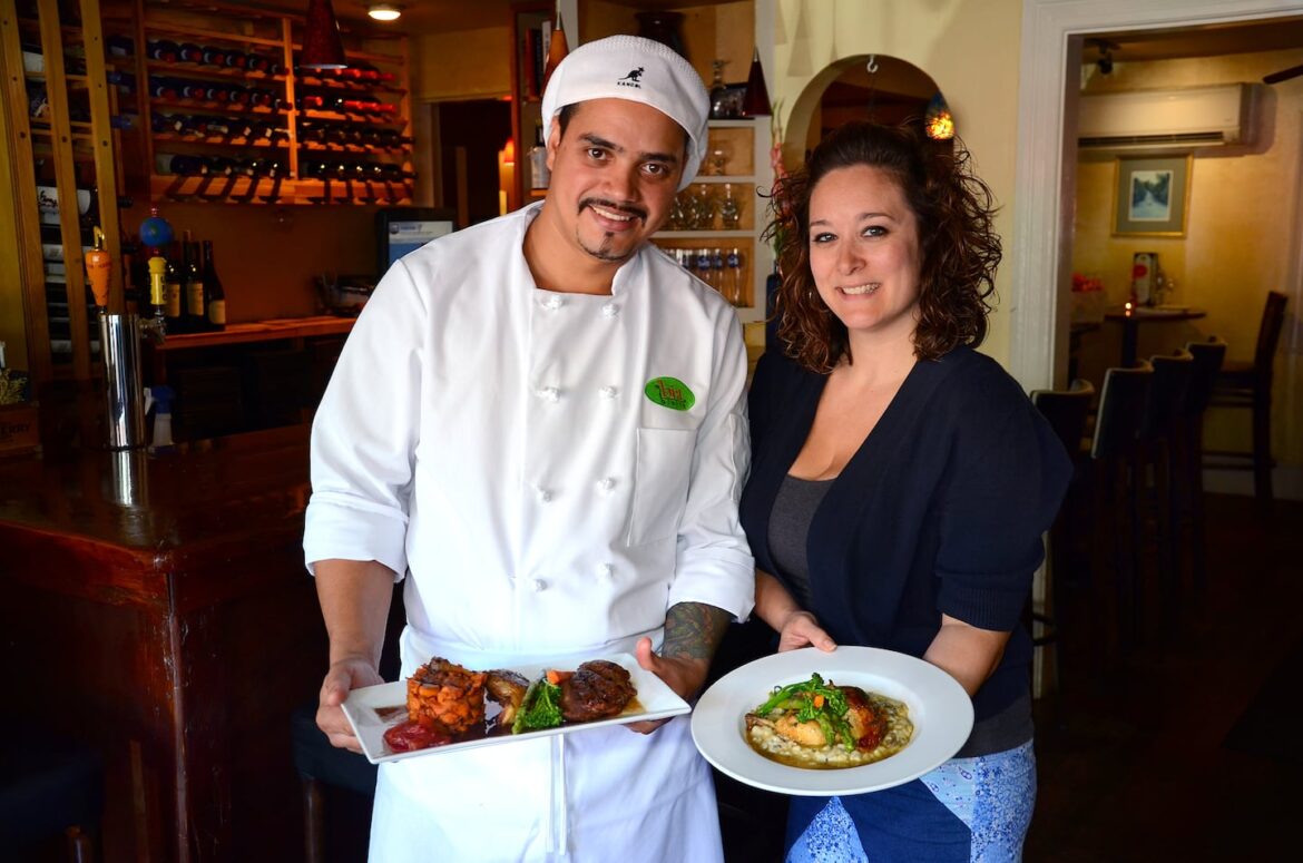 At Bia Bistro in Cohasset, satisfying French comfort food Chef Marcos DeSouza with his Citrus Glazed Long Island duck dish as manager Erica White holds the Roasted Chicken dish, at Bia Bistro in Cohasset. Photo by Debee Tlumacki for the Boston Globe
