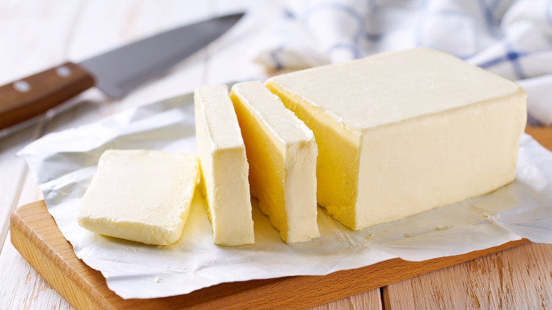 Sliced pieces of butter off a larger block, sitting on a wooden board