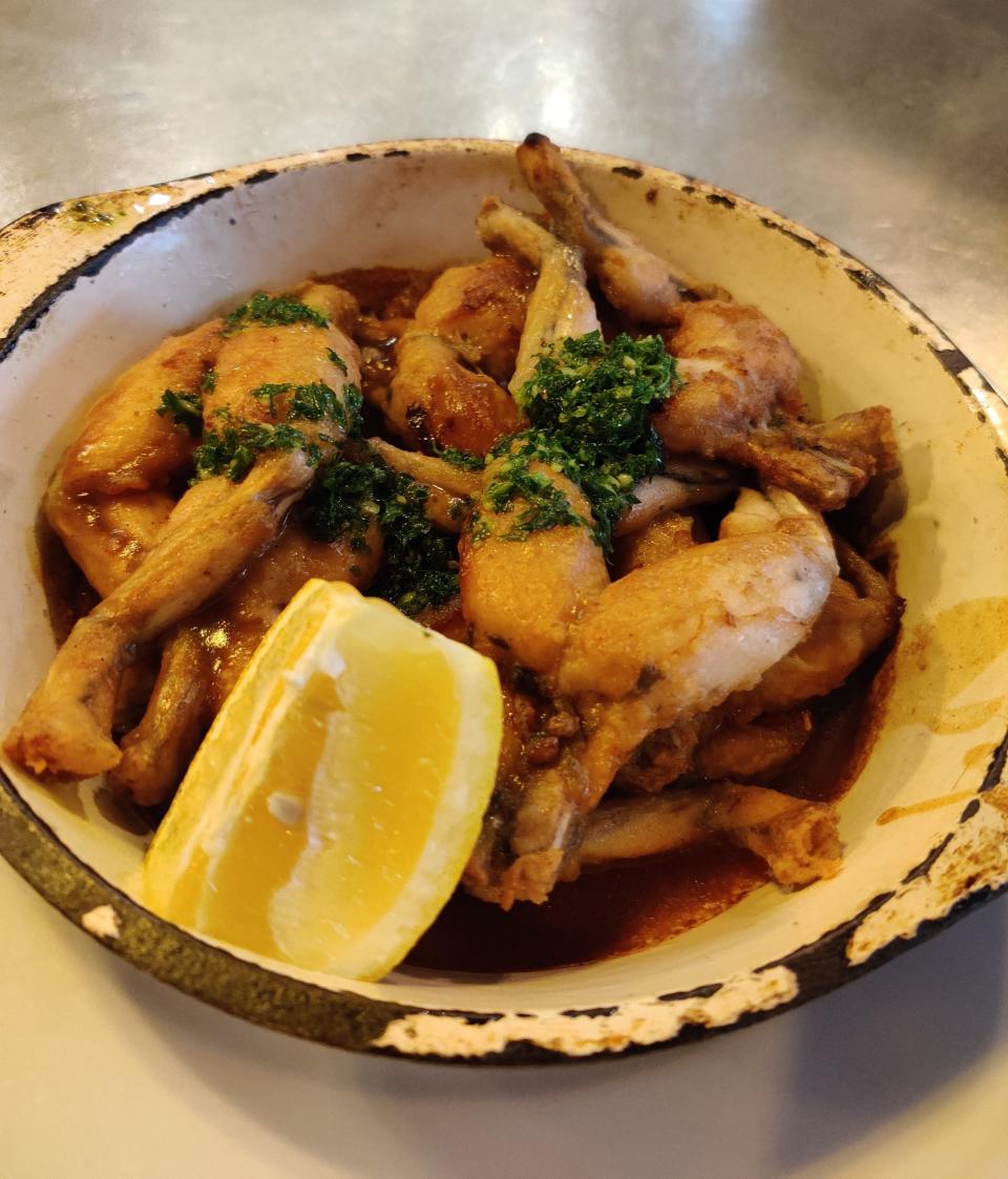 A rustic dish of frog legs garnished with green herbs and served with a lemon wedge