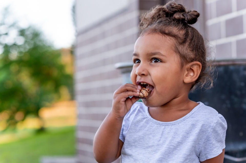 Cute little girl eating chocolate bar outdoors.