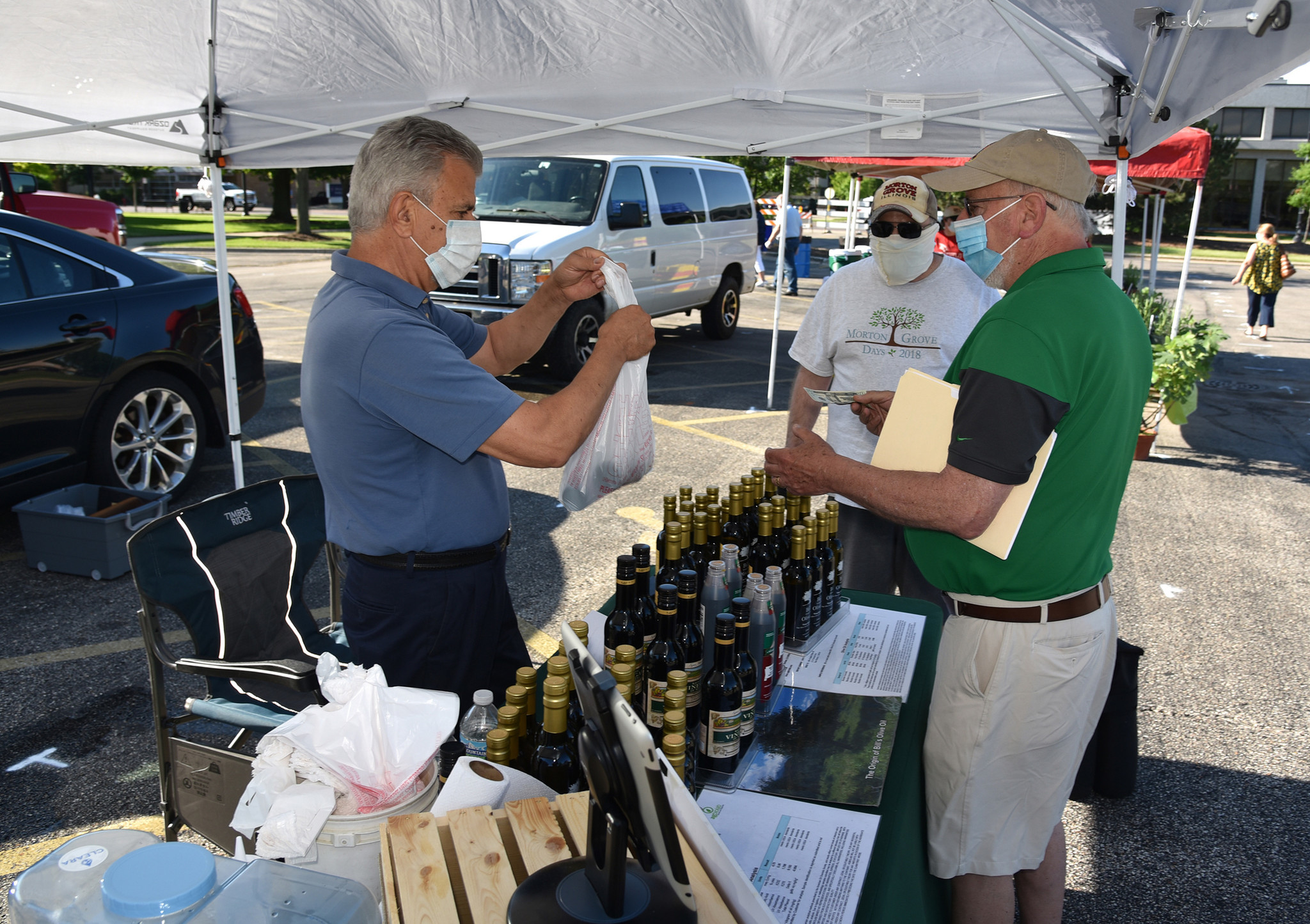 From left, olive oil vendor Bill Christakos of Des Plaines answers questions by patrons Eric Brodsky of Morton Grove and also Rich Block of Morton Grove. Images from the opening day of the Morton Grove French Market in Morton Grove on June 6, 2020 at 6140 Dempster St.