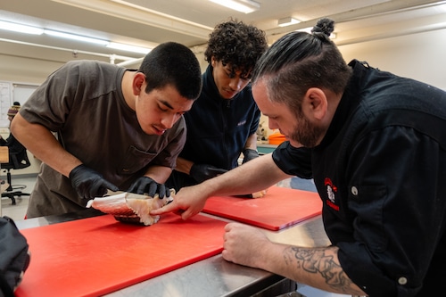 Joshua and Zion lean over a cut of fish as Patrick points at the meat of the fish