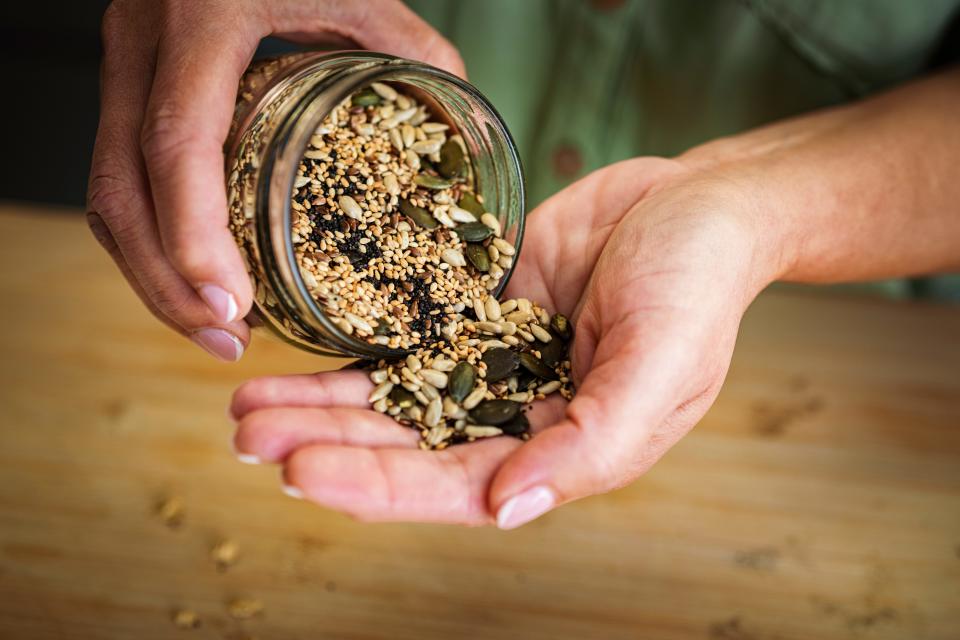 A woman pours from a jar of mixed seeds into her hand.