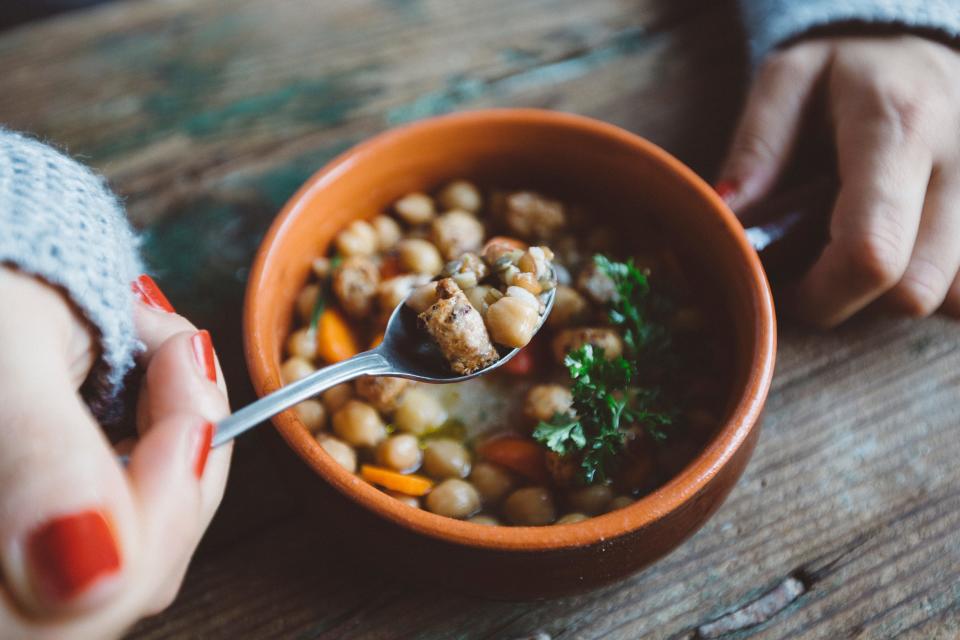A woman eats from a bowl of bean stew.