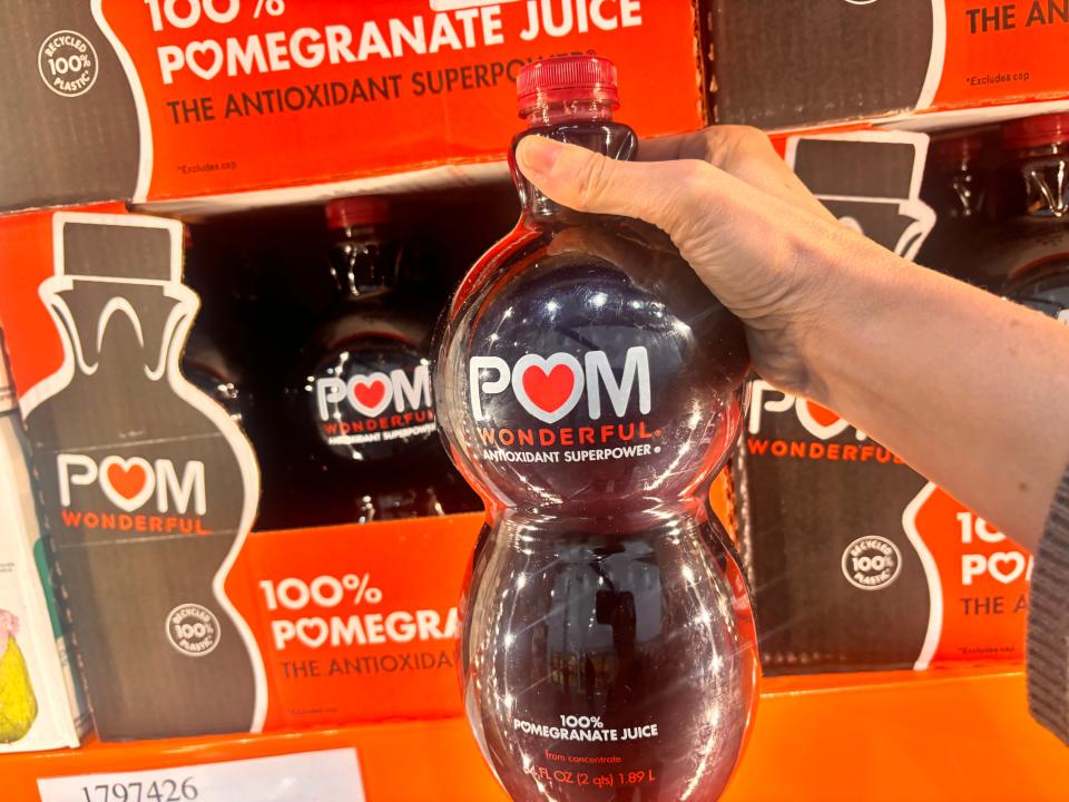 A hand holding a bottle of Pom pomegranate juice at Costco.