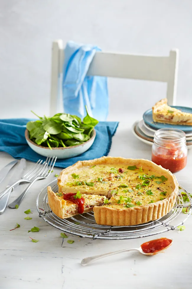 quiche lorraine still in tin with one slice cute out and salad in background