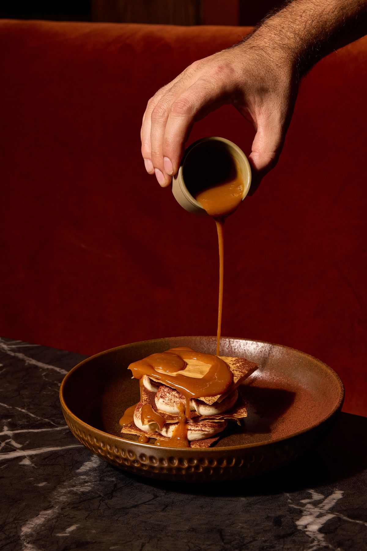 A person pours caramel on a tiramisu mille feuille at Aris.