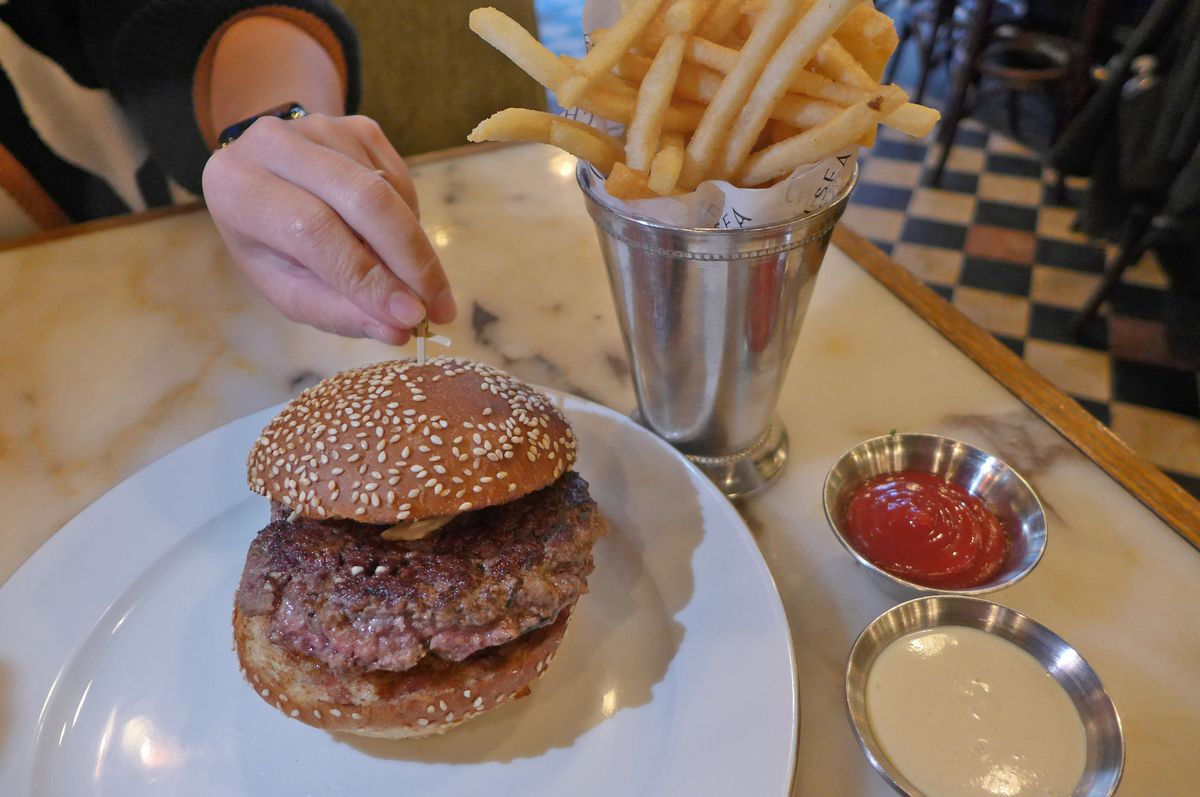 A hamburger with a seeded bun and french fries in a cone.