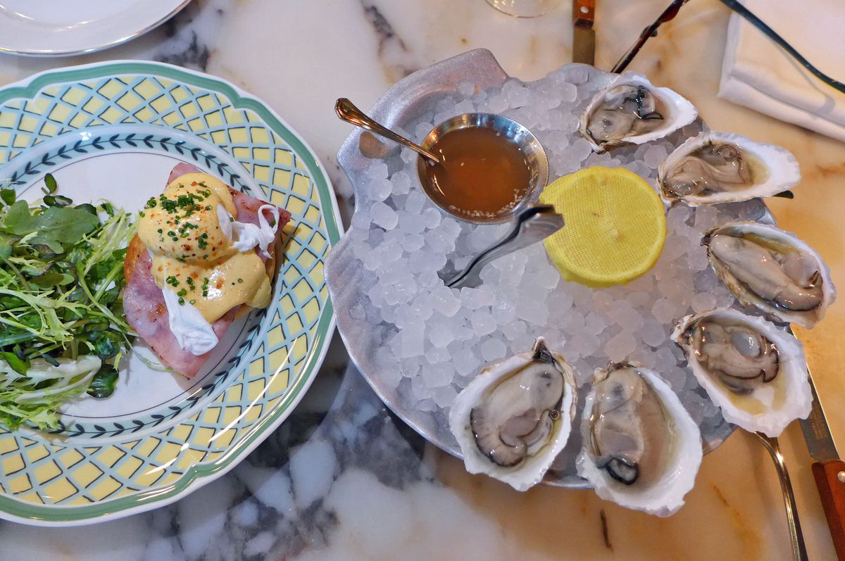 A plate with eggs benedict and a salad on the left and tray of ice with opened oysters on the right.