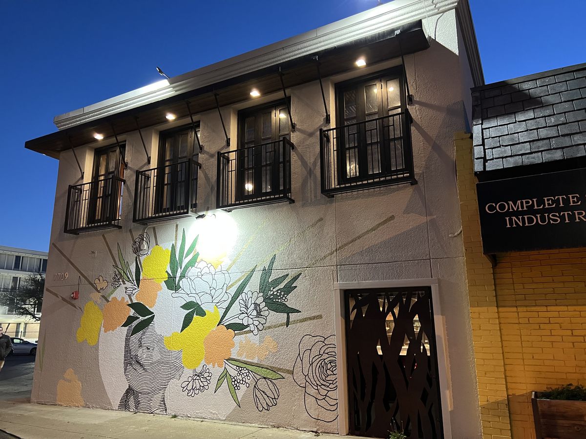 A gray building is painted with an abstract mural in white, black, tangerine, and bright yellow.
