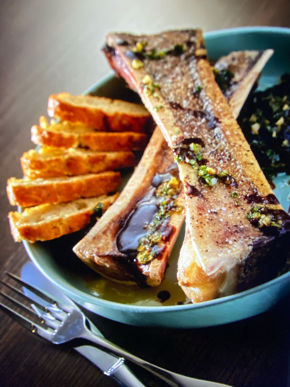 A bone sits on a light blue plate with bone marrow inside, coated in balsamic vinegar with bread on the side.