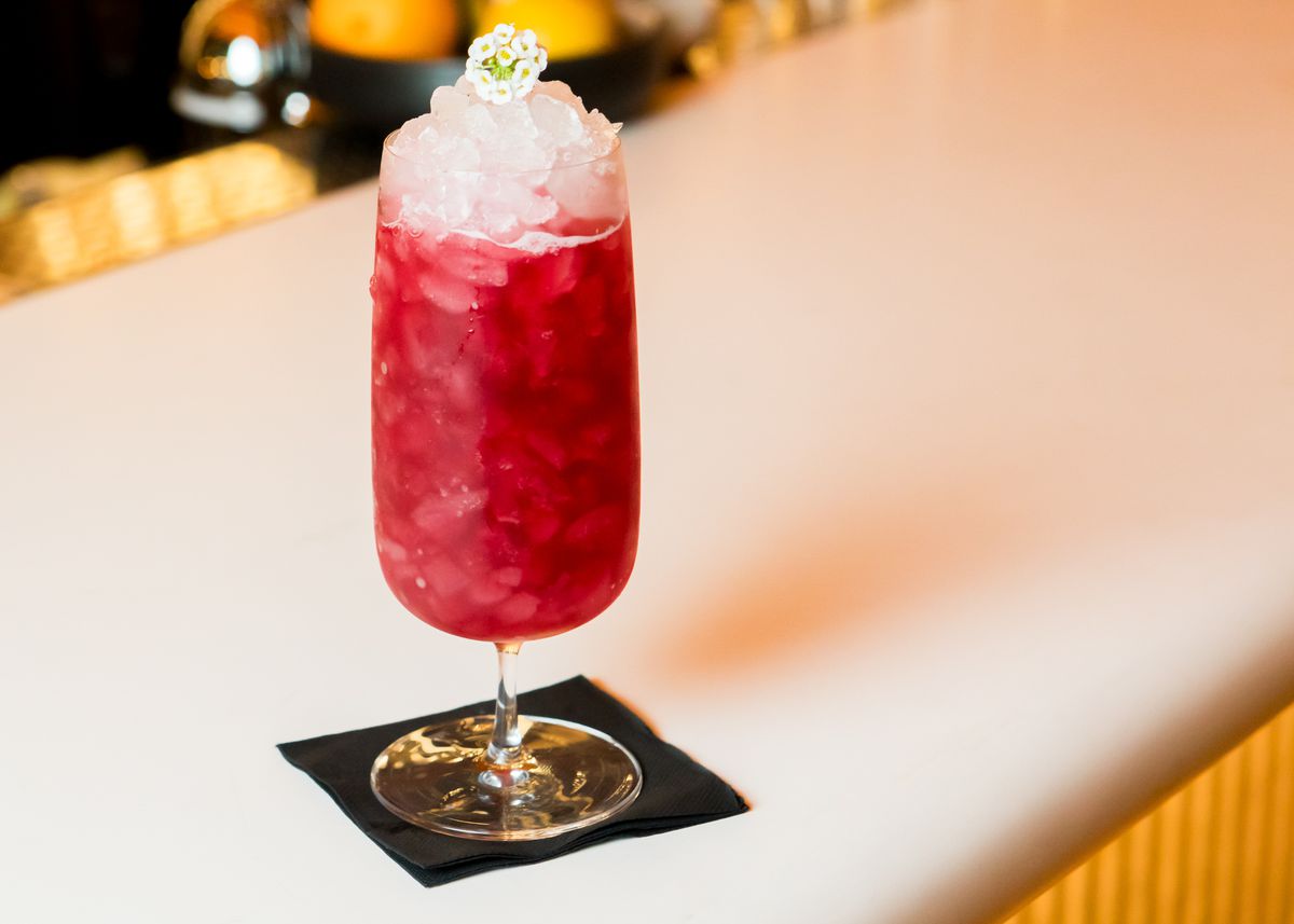 A red cocktail with crushed ice and a white flower on top.