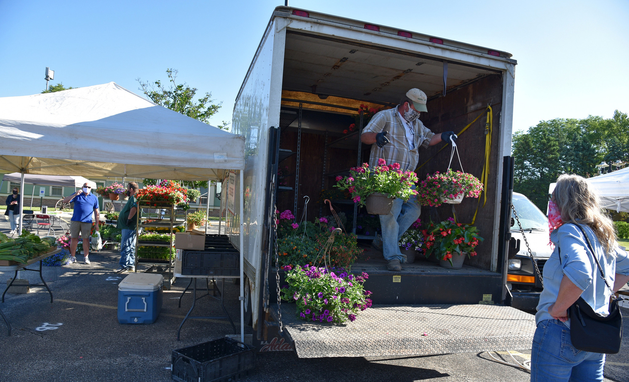 On the truck, farmer John Patyk of Richmond, IL. Patyk unloads flower basket choices for Carol Macejak, a Morton Grove resident. Patyk grew up in Morton Grove and graduated from Niles West High School. Images from the opening day of the Morton Grove French Market in Morton Grove on June 6, 2020 at 6140 Dempster St