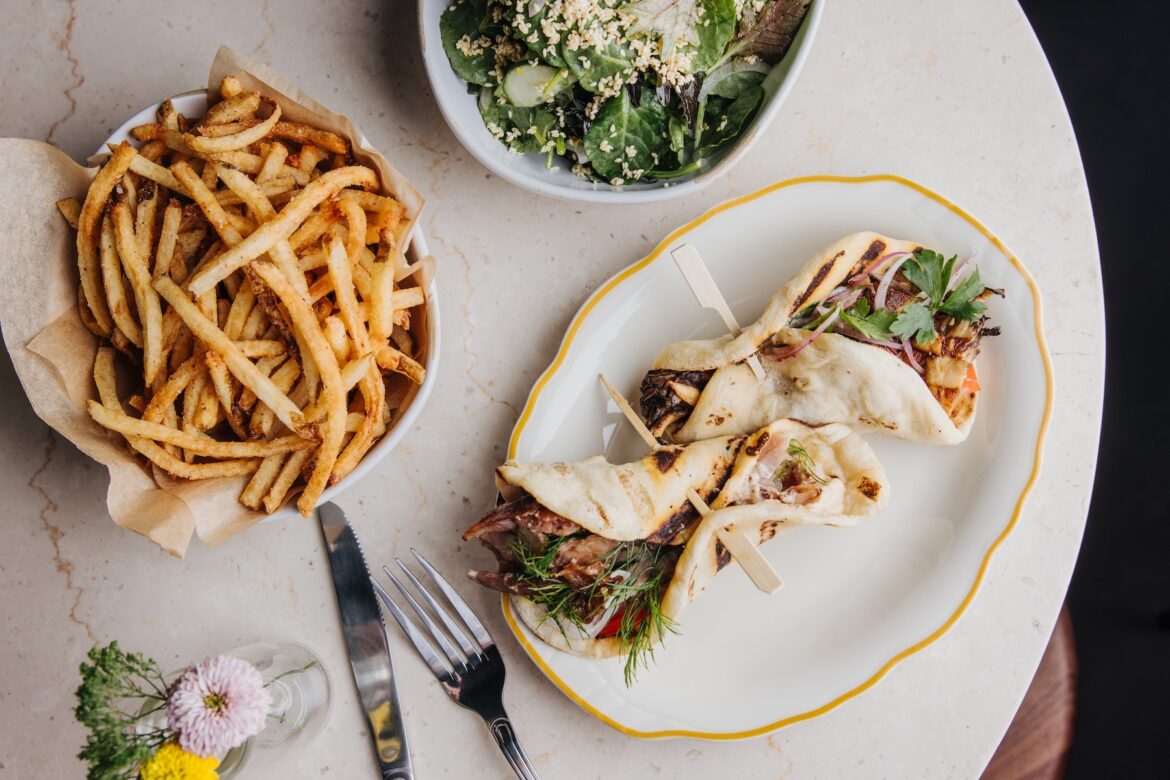 An overhead shot of several greek food platters, like gyros, fries and a salad with feta cheese.