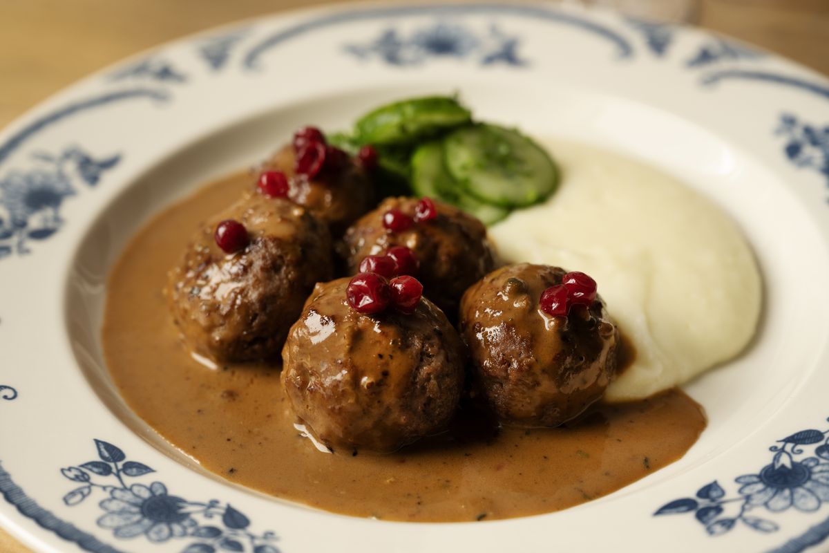 A plate of meatballs, with a cream sauce, sliced cucumbers, and a brown sauce.