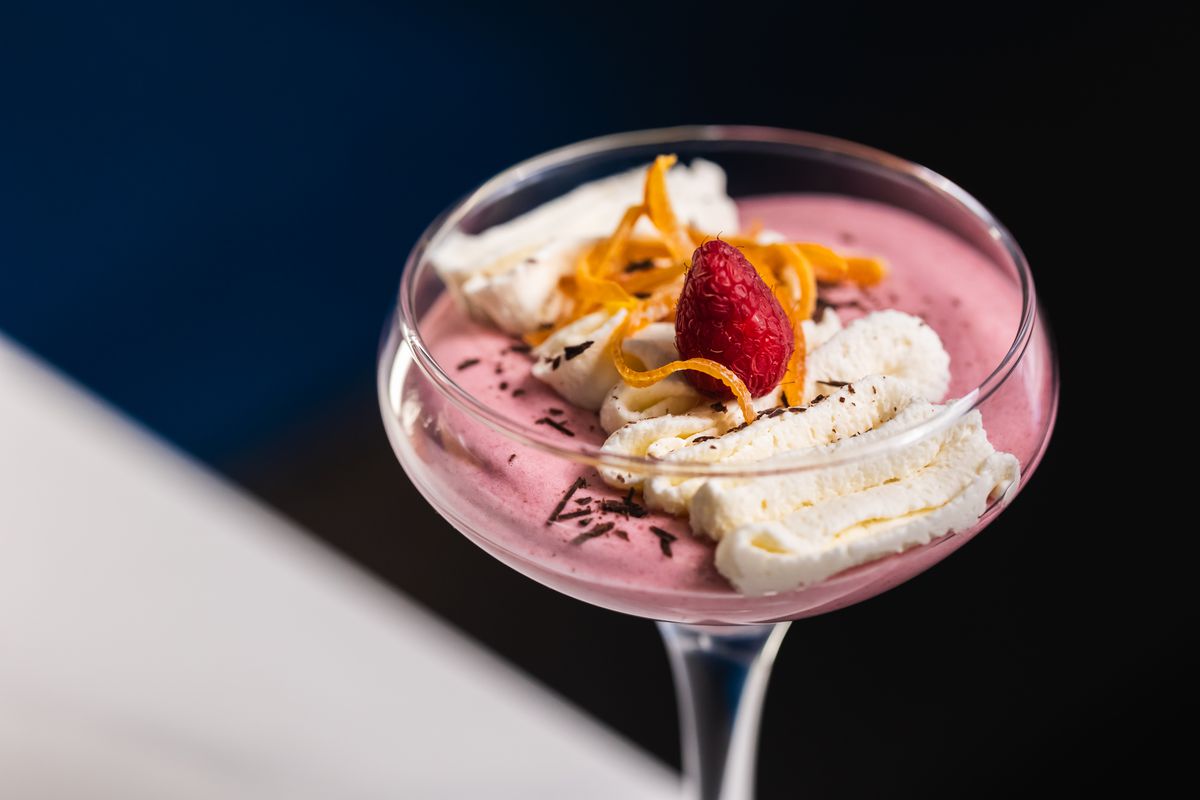 A coupe glass with pink mousse and cream and a raspberry.