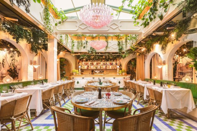 interiors of italian restaurant Jacuzzi where you can see chandeliers hanging from the open ceiling with natural light coming in, green vines and tables and chairs set