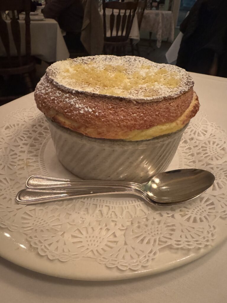 A lemon soufflé sits on a doilie at a restaurant. It is plated with two spoons.