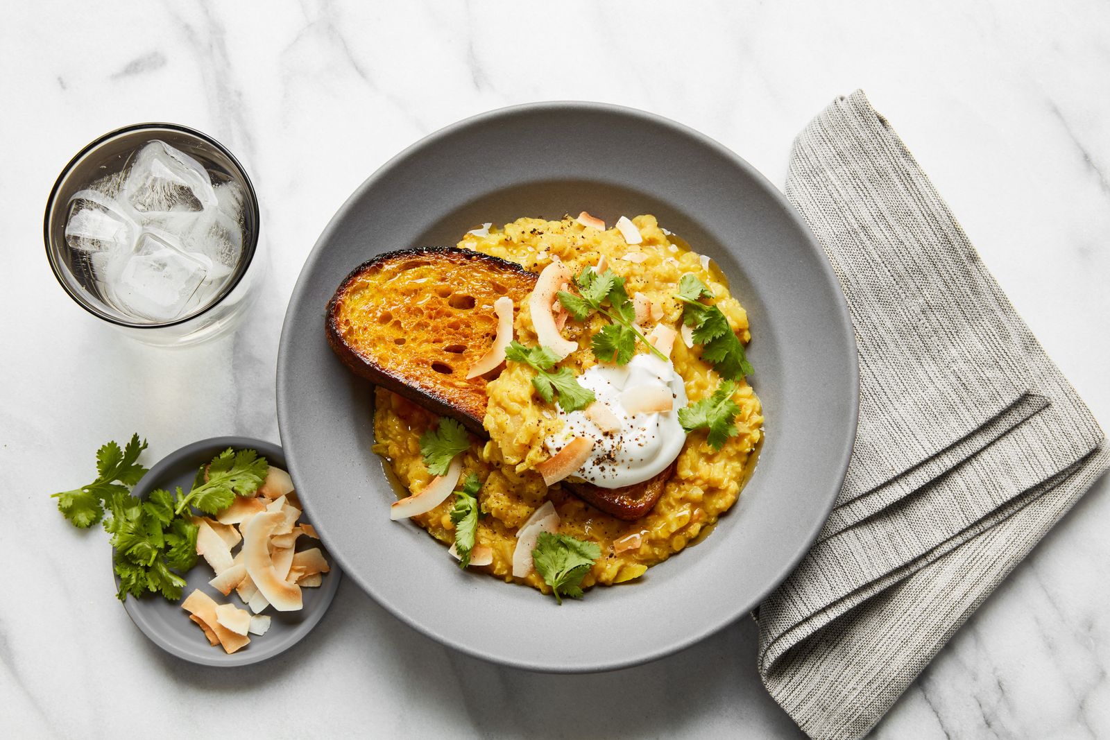 Photo of lentils on toast in a bowl a dollop of cream and cilantro on top.