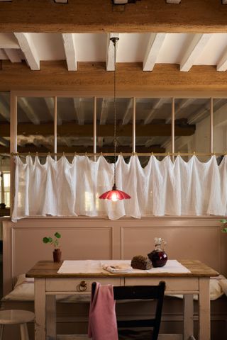 French bistro style kitchen with wooden beams, cafe curtains, wooden dining table and low pendant vintage light