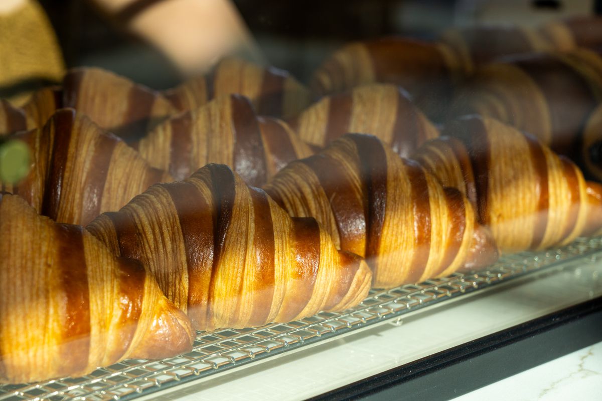 Freshly baked croissants on a rack in a glass case.