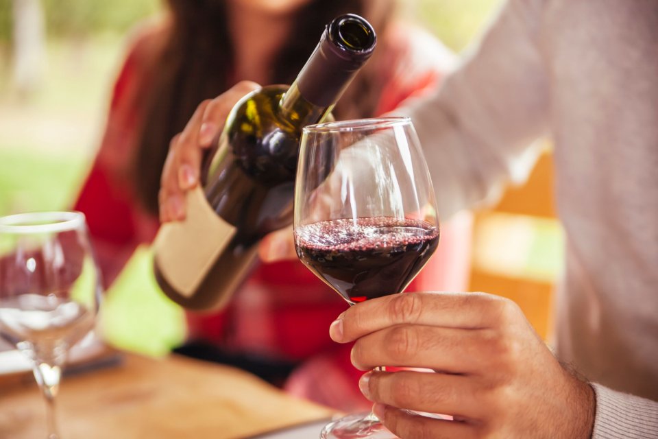 Person pouring red wine into a glass.