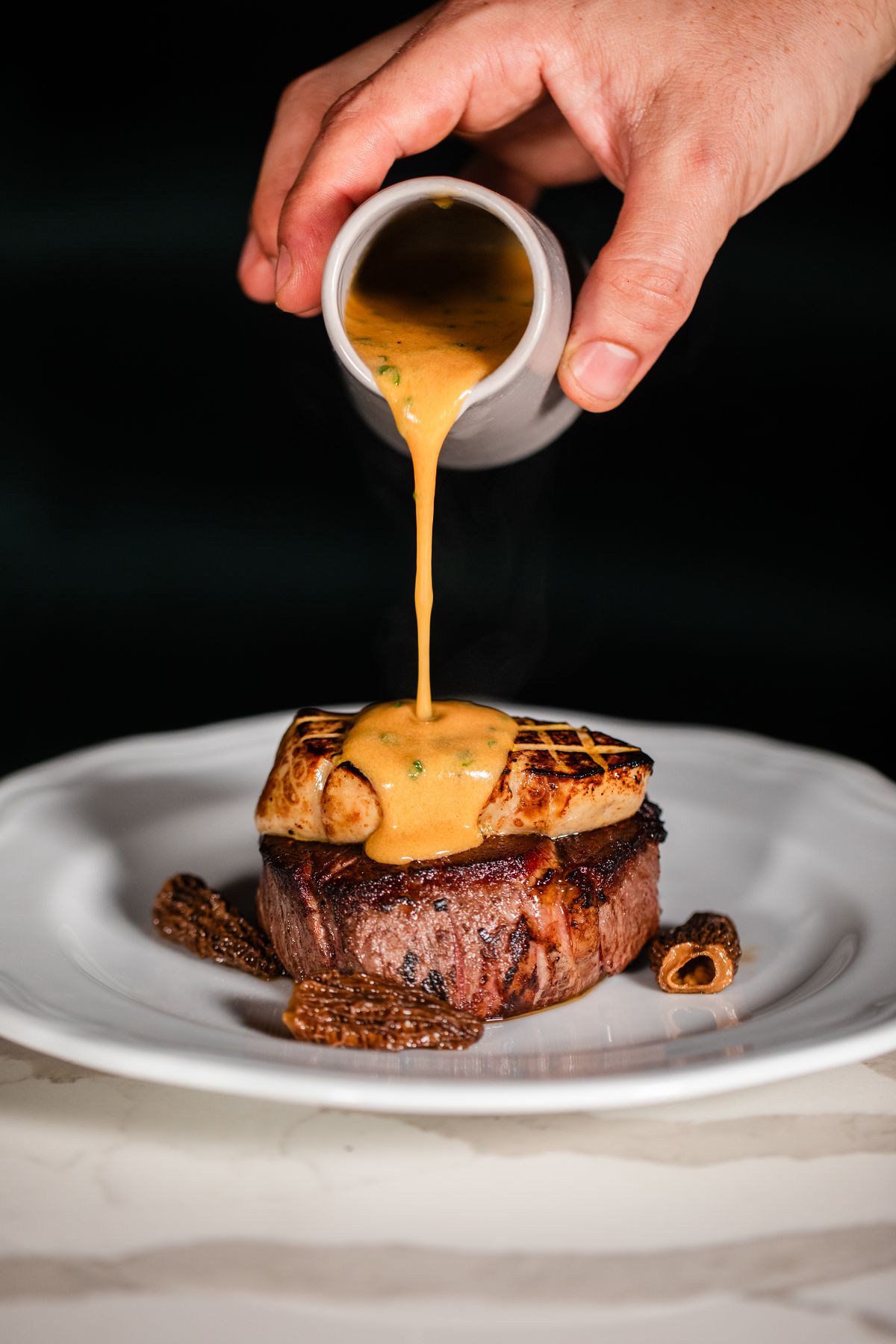 A person pours sauce atop steak Rossini with foie gras at Okto.