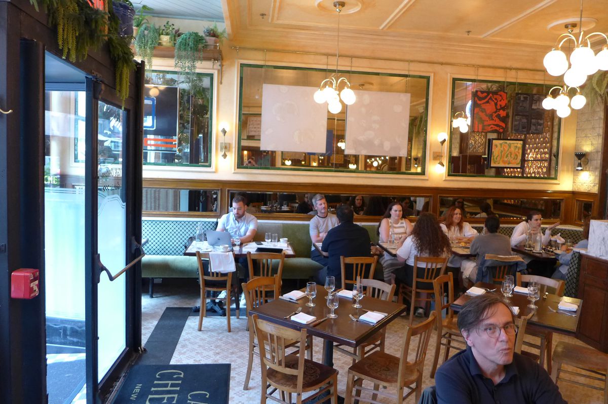 A light room with wooden chairs and tables, with one diner staring directly at the camera.