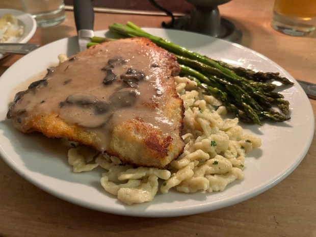 A breaded pork tenderloin atop dumplings with asparagus on the side