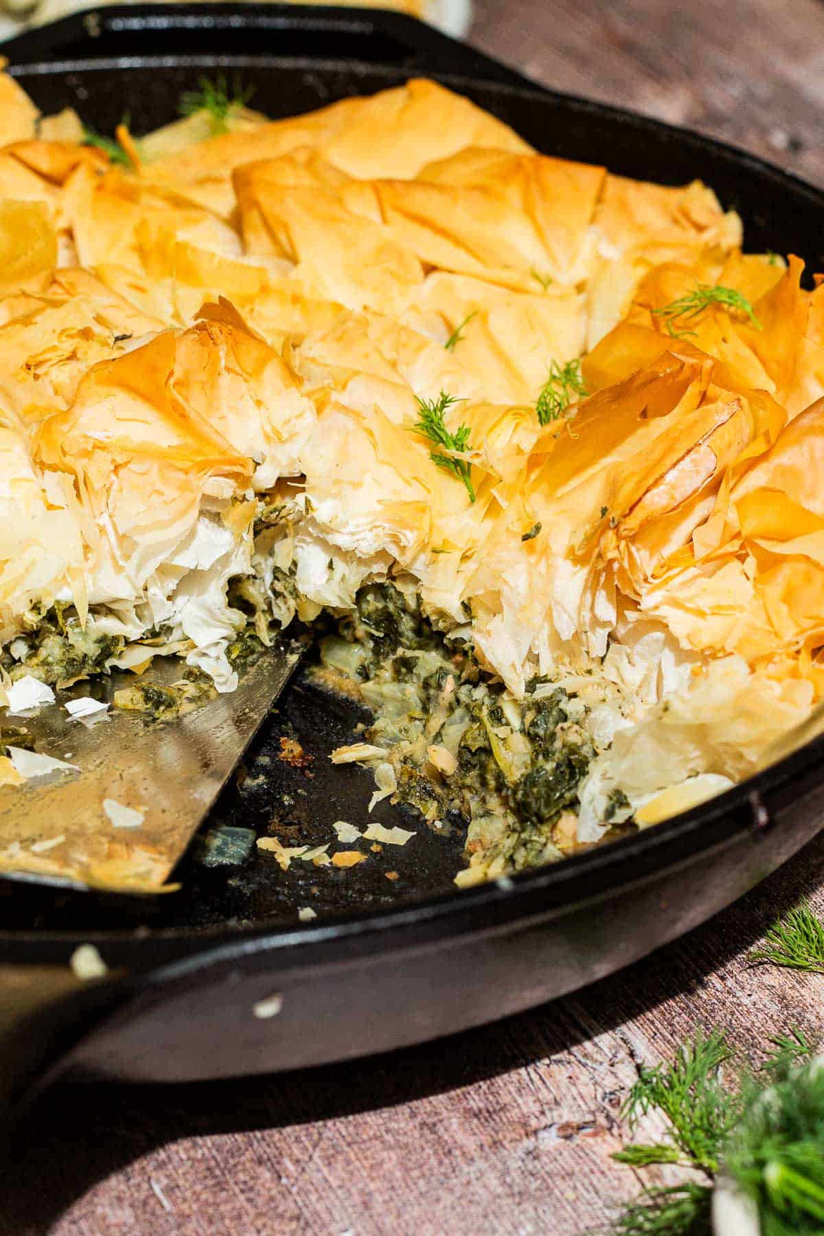 A close up of vegan skillet spanakopita in a skillet with one slice removed.