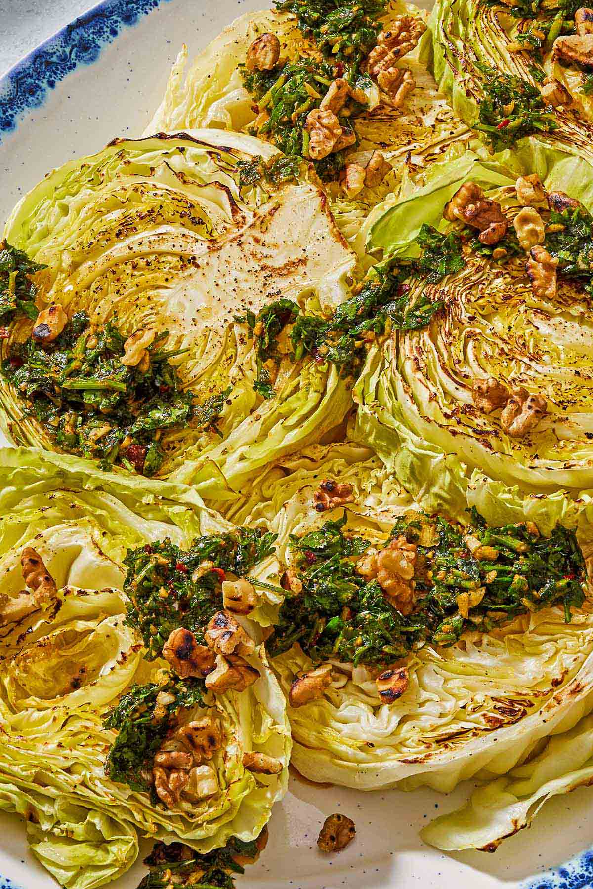 A close up of cabbage steaks topped with green chermoula and toasted walnuts on a serving platter.