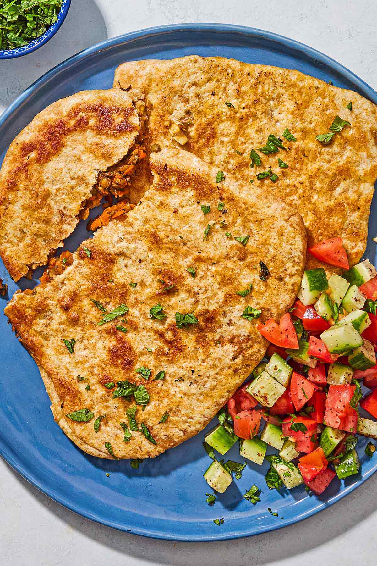 Stuffed flatbreads filled with harissa carrots and lentils on a plate with a cucumber tomato salad.