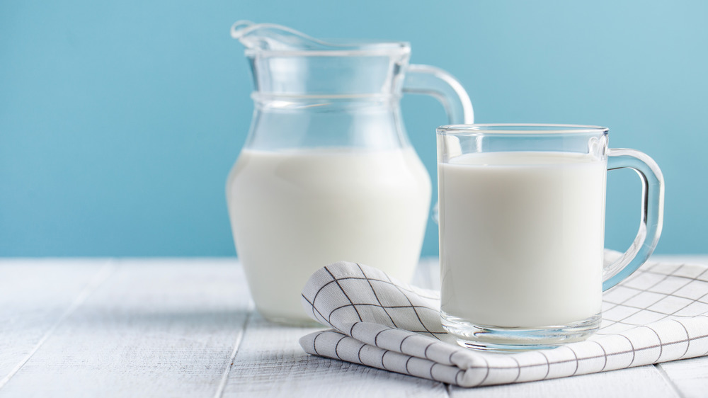 A pitcher of milk next to a glass of milk on a napkin.