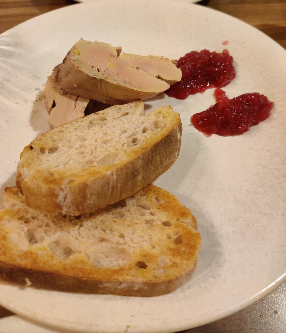 Slices of bread and foie gras with two dollops of red jam on a white plate