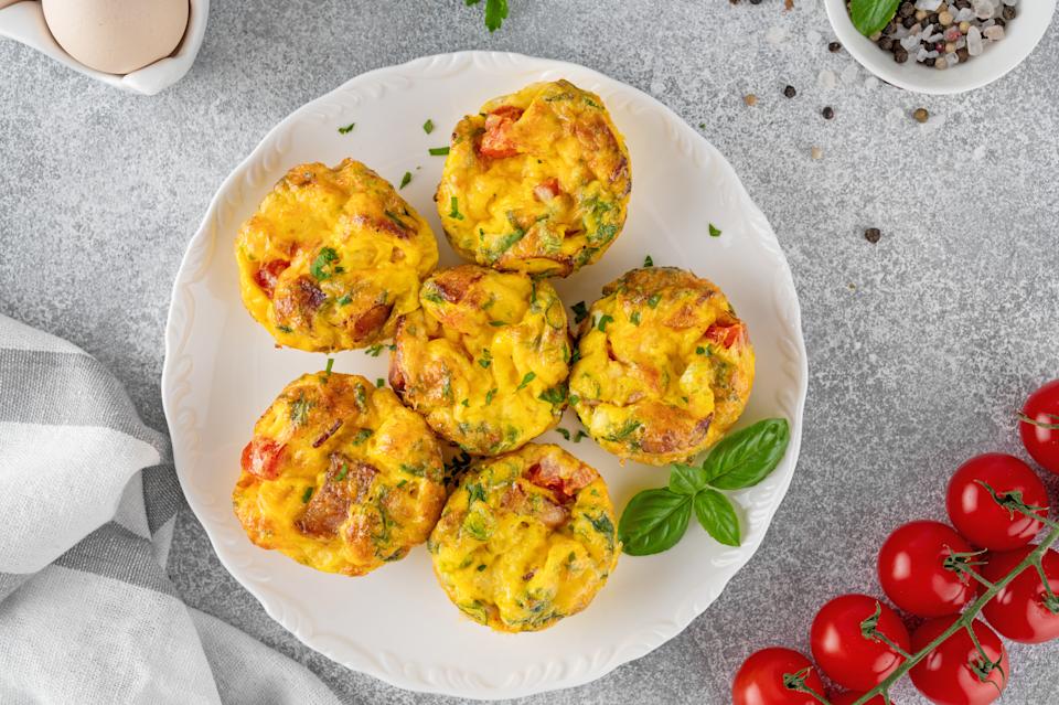 Egg muffins or egg bites with bacon, cheese, vegetables and herbs on a white plate on a concrete background. Healthy breakfast